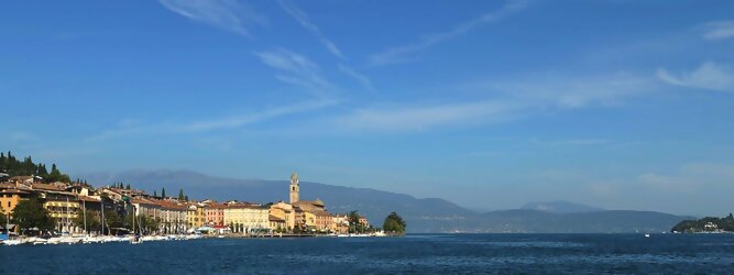 Trip Russia beliebte Urlaubsziele am Gardasee -  Mit einer Fläche von 370 km² ist der Gardasee der größte See Italiens. Es liegt am Fuße der Alpen und erstreckt sich über drei Staaten: Lombardei, Venetien und Trentino. Die maximale Tiefe des Sees beträgt 346 m, er hat eine längliche Form und sein nördliches Ende ist sehr schmal. Dort ist der See von den Bergen der Gruppo di Baldo umgeben. Du trittst aus deinem gemütlichen Hotelzimmer und es begrüßt dich die warme italienische Sonne. Du blickst auf den atemberaubenden Gardasee, der in zahlreichen Blautönen schimmert - von tiefem Dunkelblau bis zu funkelndem Türkis. Majestätische Berge umgeben dich, während die Brise sanft deine Haut streichelt und der Duft von blühenden Zitronenbäumen deine Nase kitzelt. Du schlenderst die malerischen, engen Gassen entlang, vorbei an farbenfrohen, blumengeschmückten Häusern. Vereinzelt unterbricht das fröhliche Lachen der Einheimischen die friedvolle Stille. Du fühlst dich wie in einem Traum, der nicht enden will. Jeder Schritt führt dich zu neuen Entdeckungen und Abenteuern. Du probierst die köstliche italienische Küche mit ihren frischen Zutaten und verführerischen Aromen. Die Sonne geht langsam unter und taucht den Himmel in ein leuchtendes Orange-rot - ein spektakulärer Anblick.